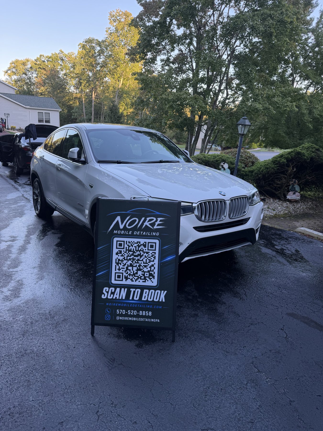 White BMW SUV detailed by Noire Mobile Detailing with scan to book sign